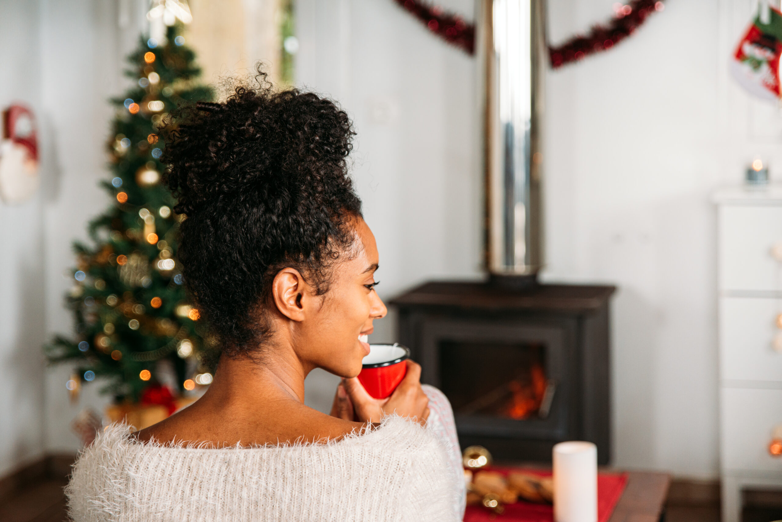 Woman enjoying a hot drink by the fireplace during the holiday season, preparing her smile with a pre-holiday dental checkup.