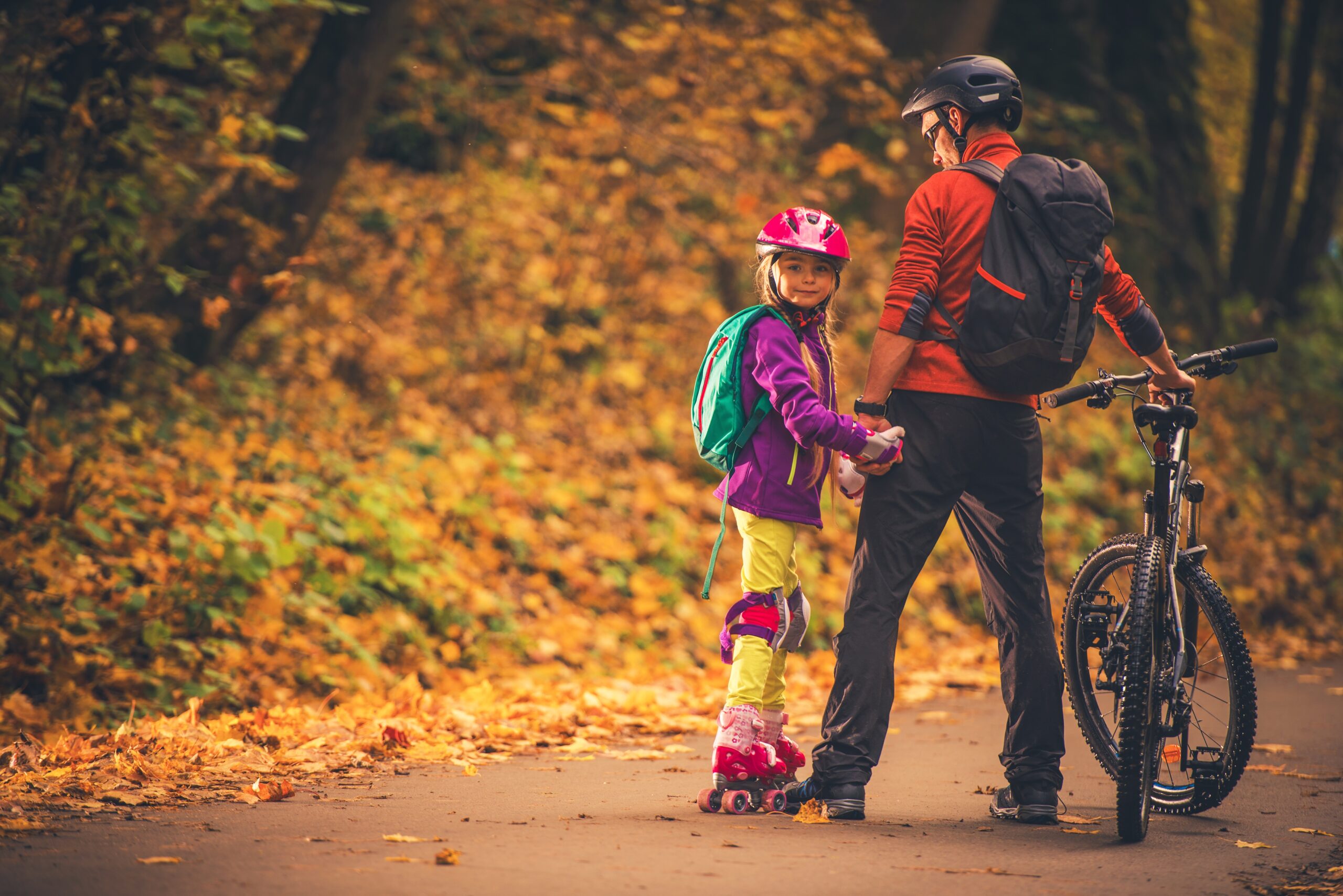 Father and daughter enjoying a fall day outdoors while biking and roller skating, representing seasonal transitions and healthy habits.